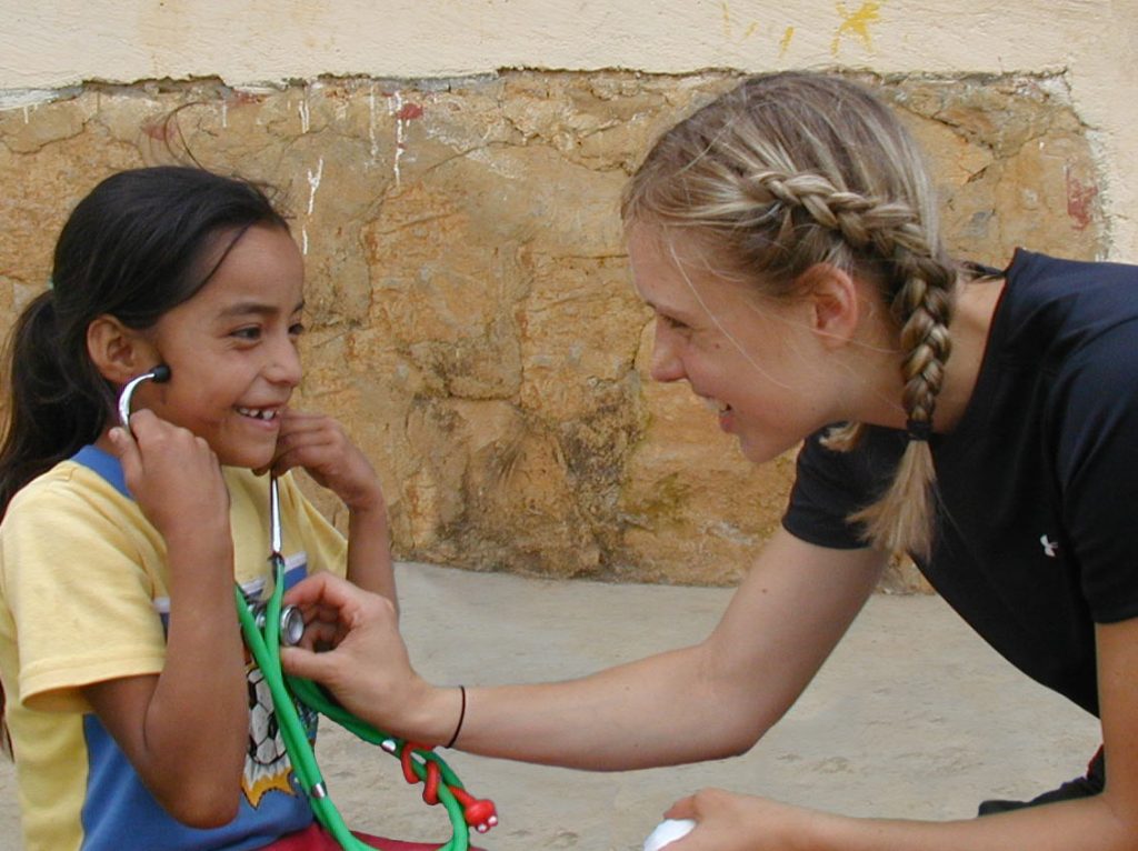 A happy volunteer nurse showing a little girl how to listen to her heartbeat