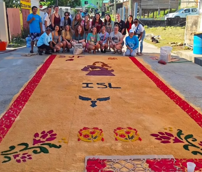 Group of volunteers taking a photo as a group with a painting of ISL on the ground