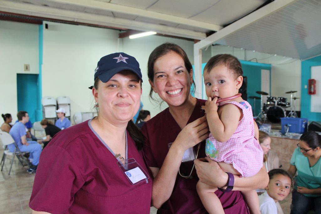 Two volunteer nurses holding a baby and smiling