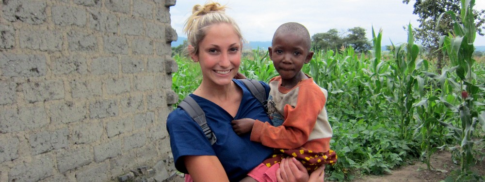 A volunteer nurse carrying a child and smiling for a photo