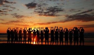 A silhouette of a large group of people with the ocean and sunset in the background